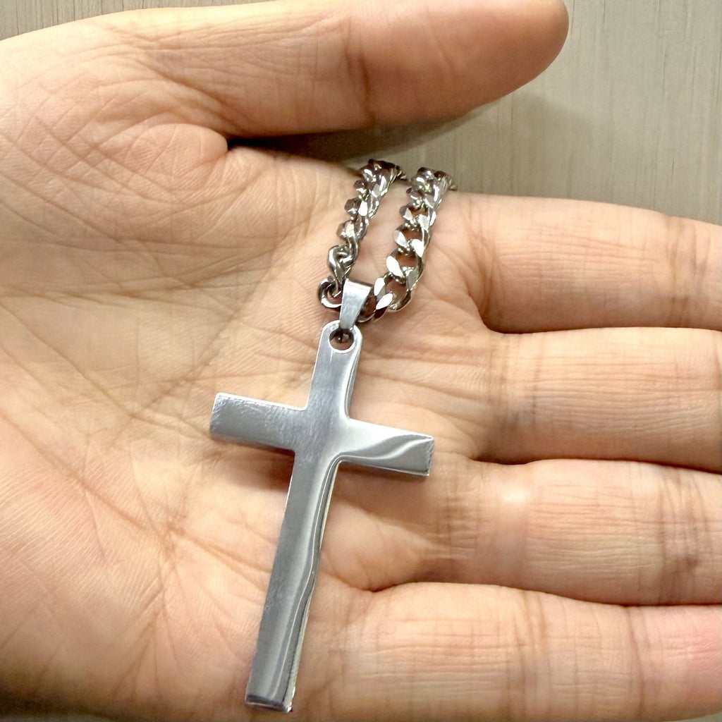 Silver cross pendant necklace held in a hand to show its size