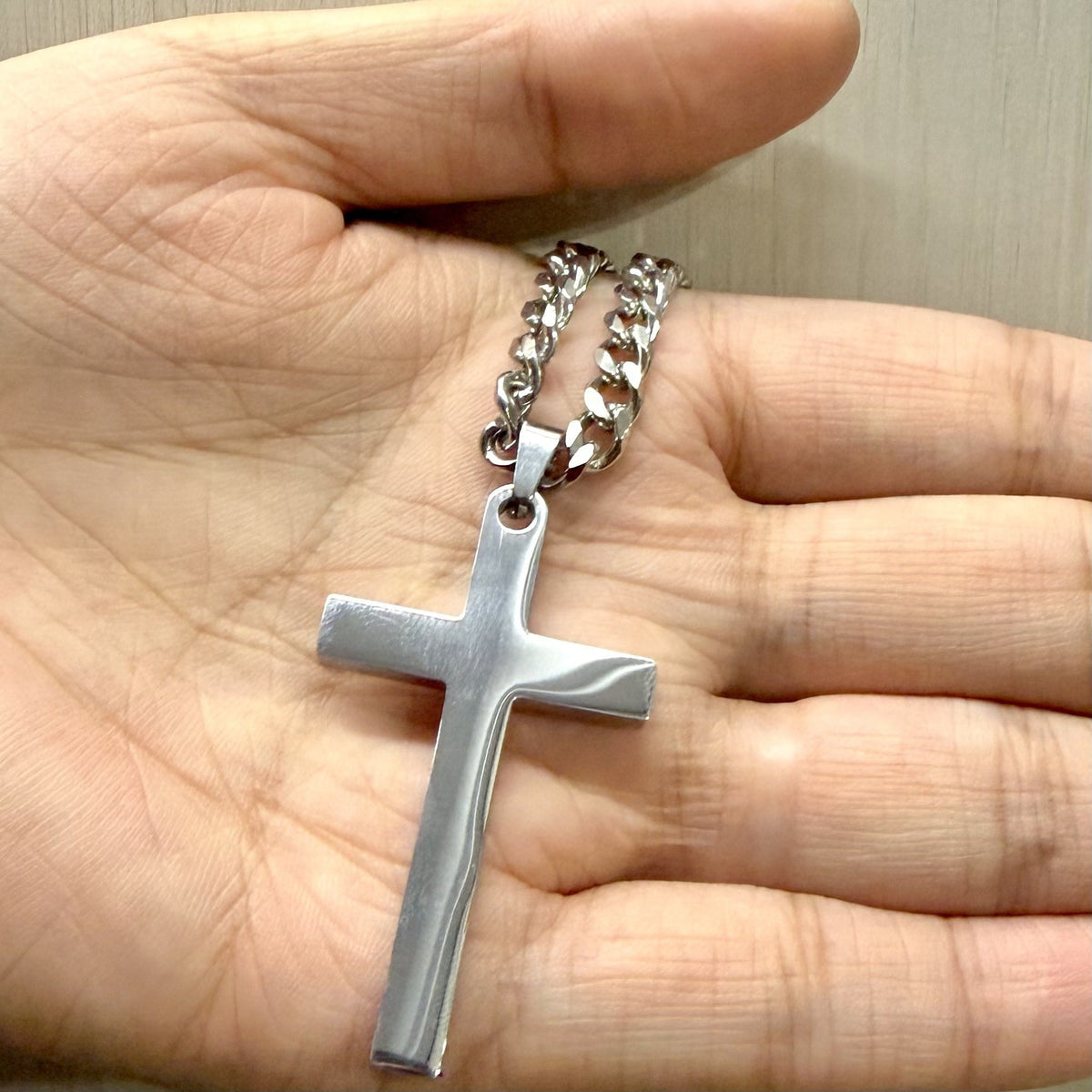 Silver cross pendant necklace held in a hand to show its size
