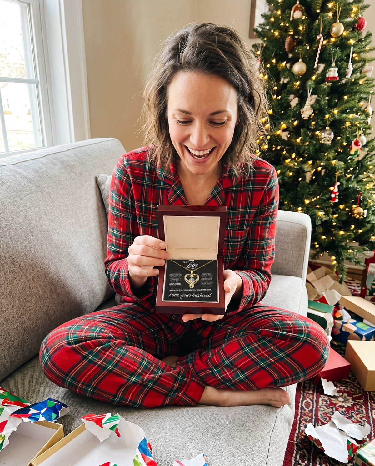 Woman smiling on Christmas morning as she opens The Eternal Heart necklace in a luxury wood gift box with a 'To My Love' card from her husband
